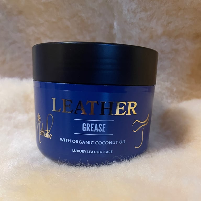 Blå beholder med sort låg mærket "Leather Grease with organic coconut oil luxury leather care" placeret på en blød, hvid overflade.