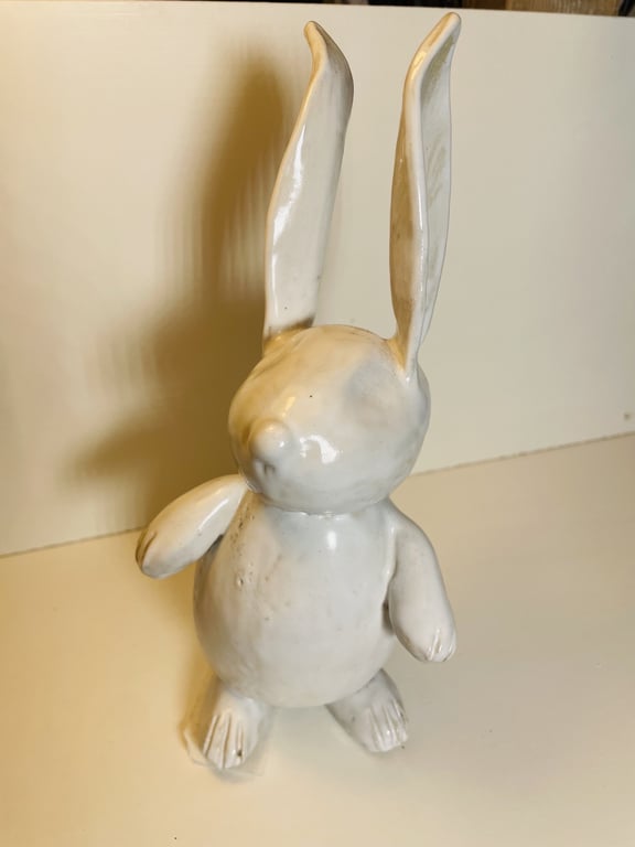 Keramisk hvid kaninfigur med store opretstående ører stående på en lys overflade mod en lys baggrund.
