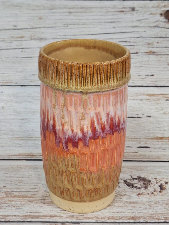Keramisk vase med glaserede, jordfarvede nuancer i brunt, orange og rødt, stående på træbund.