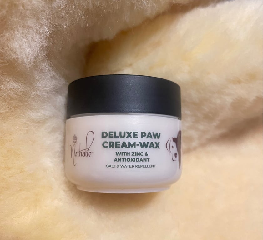 Boks med Deluxe Paw Cream-Wax til hunde, placeret på blødt, beige stof.