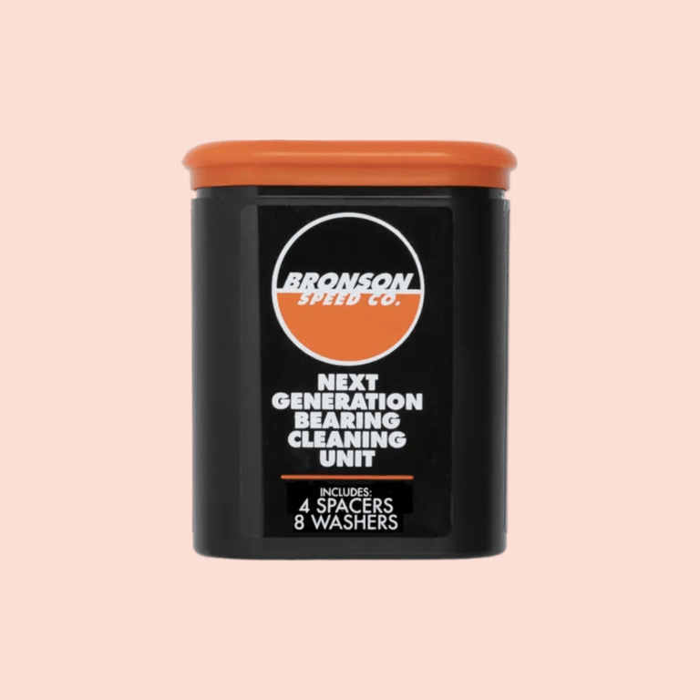 Sort og orange Bronson Speed Co. enhed til rengøring af kuglelejer med tekst på forsiden mod lyserød baggrund.
