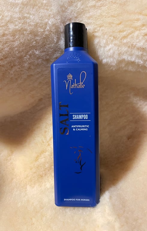 Blå flaske med Nathalie Salt shampoo til heste, placeret på en beige uldplaid.