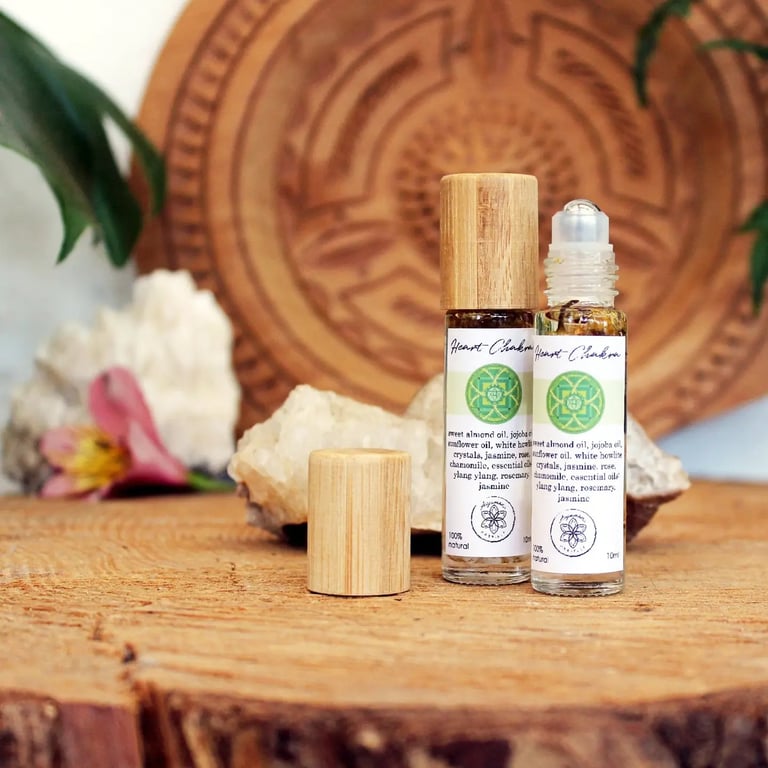 To små glasflasker med ruller, der indeholder naturlig olie, står på et træbord med en dekoreret træplade, krystaller og blomster i baggrunden. (4)