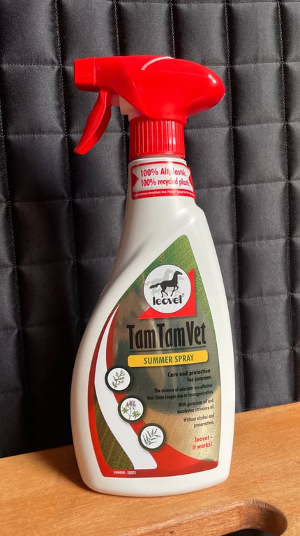 Flaske med rød sprayhoved med teksten "Tam Tam Vet Summer Spray" på label mod mørk quiltet baggrund.