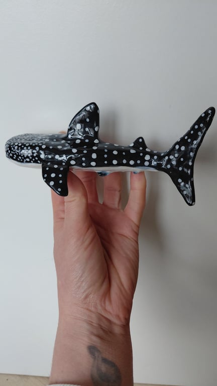 Hånd der holder en sort og hvidplettet model af en hvalhaj mod en lys baggrund.