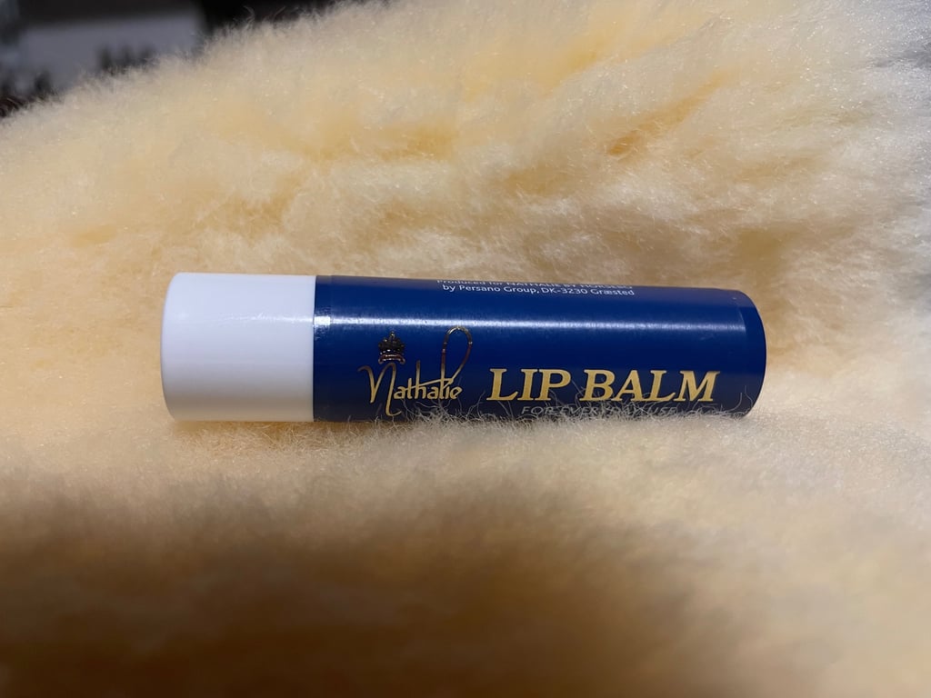 Blå læbepomade med hvid hætte liggende på blødt, lyst, gul-agtigt stof.
