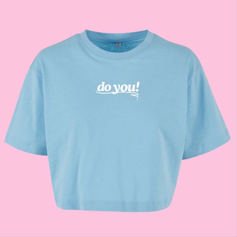 Lyseblå cropped T-shirt med hvid tekst "do you!" på brystet mod lyserød baggrund.