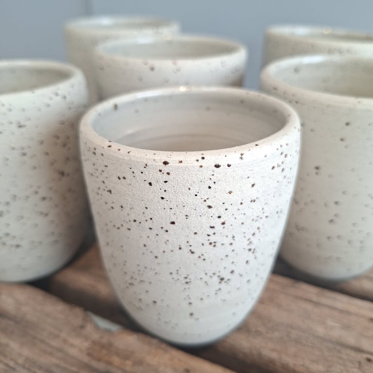 Sekskantede, hvide keramikkrus med sorte prikker, placeret på en træoverflade.