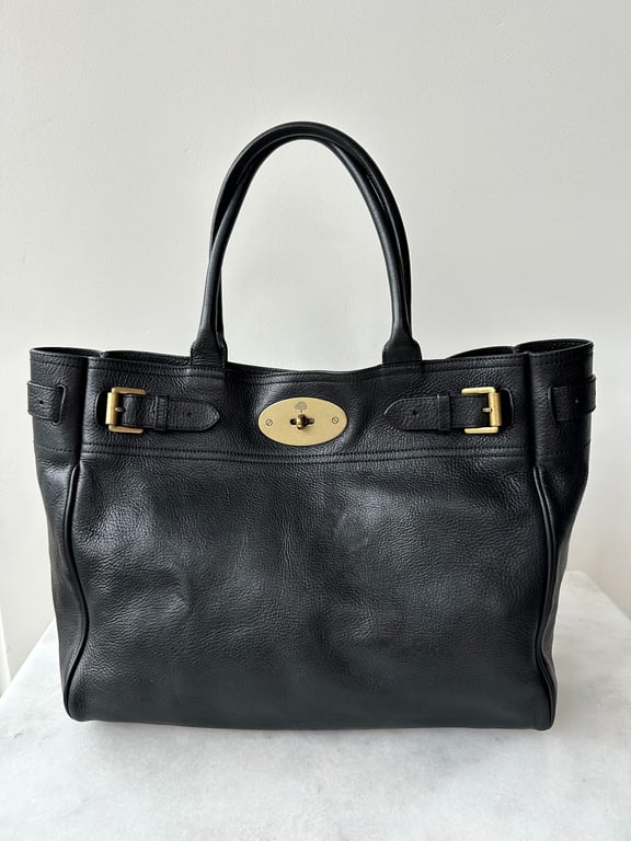 Sort lædertaske med to håndtag og gyldent spænde foran, placeret på hvid overflade mod hvid baggrund.