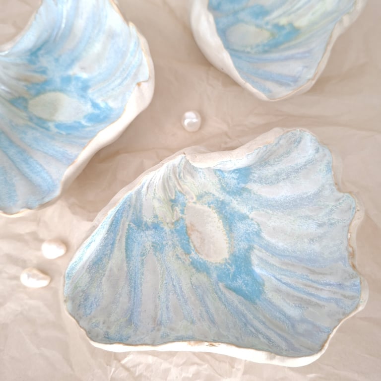 Tre blå-hvide keramiske skaller med blanke hvide perler på beige baggrund.