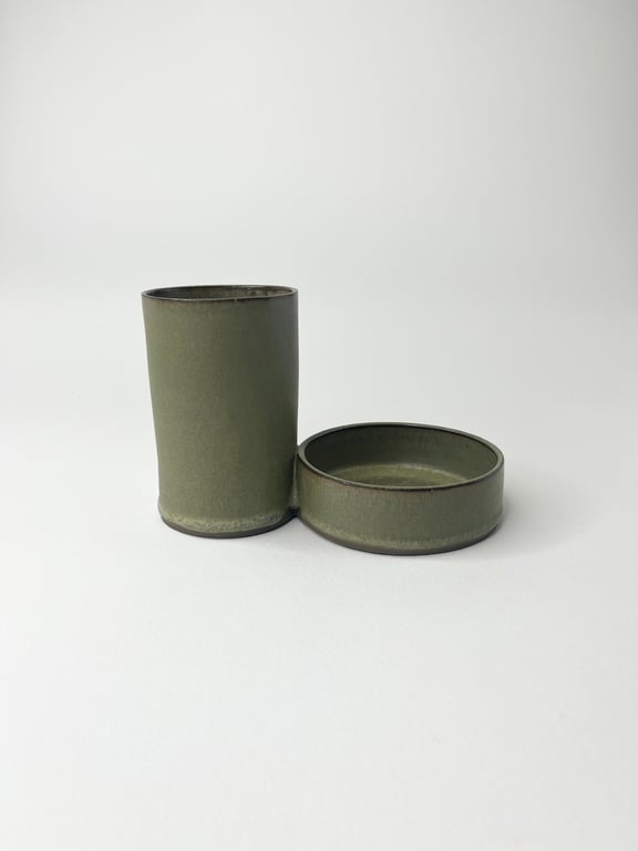 To-delt grønt keramik sæt med en høj cylinderformet beholder og en lav, rund skål, placeret på en hvid baggrund.