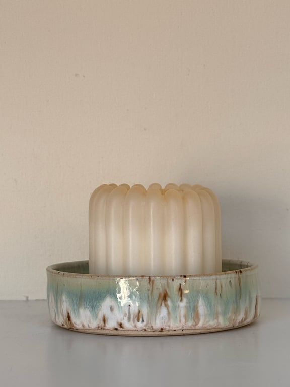 Hvid ribbet bloklys placeret i en rund keramisk lysestage med blågrønne og brune glasurdetaljer.