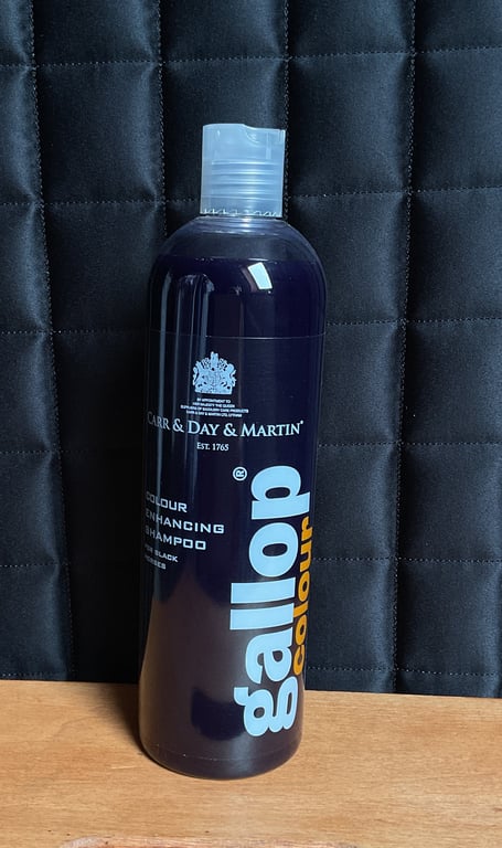 Flaske med Gallop Colour Colour Enhancing Shampoo i sort, placeret på en træbordplade foran en sort quiltet baggrund.