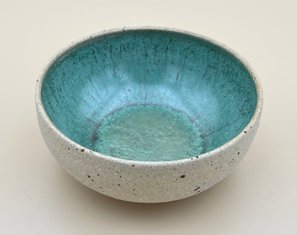 Skål med grå yderside og blank turkis inderside, placeret på en beige overflade.