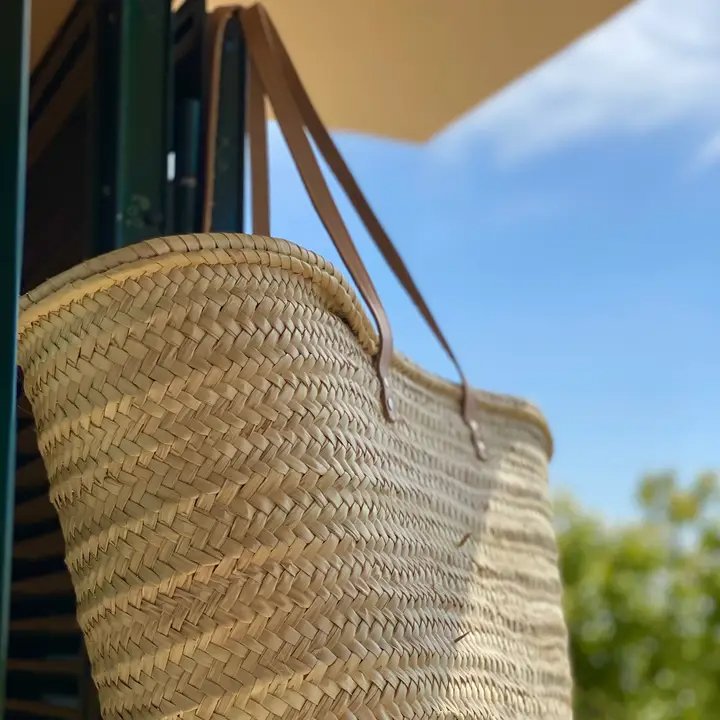 Flettet halmbuket taske med læderhanke hængende under en parasol mod en blå himmel. (2)