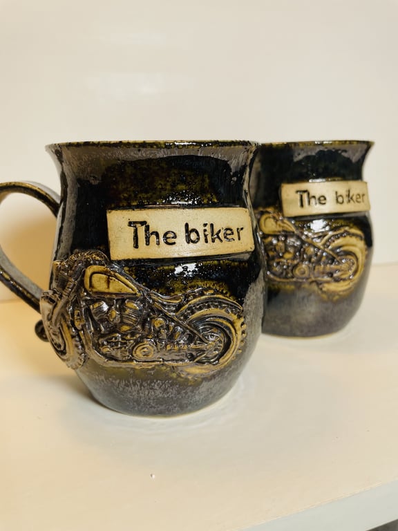 To sorte keramikkrus med relief af en motorcykel og teksten "The biker" på forsiden.