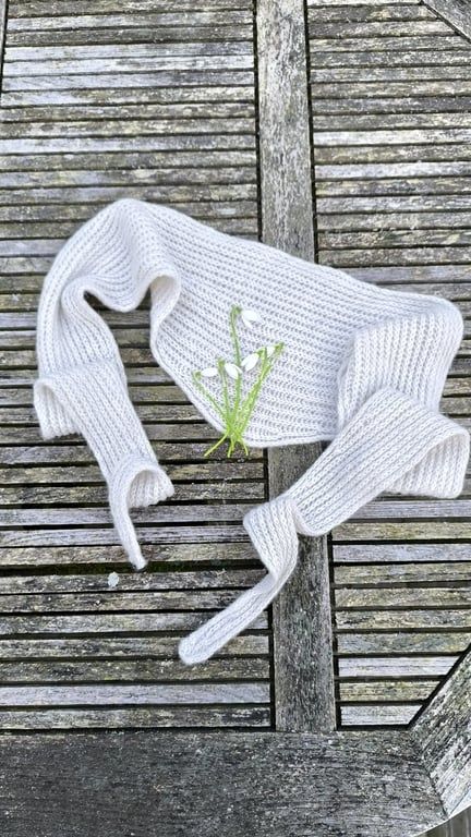 Hvidt strikket tørklæde lagt på vejrslidt træbord med små hvide sneklokke blomster på.