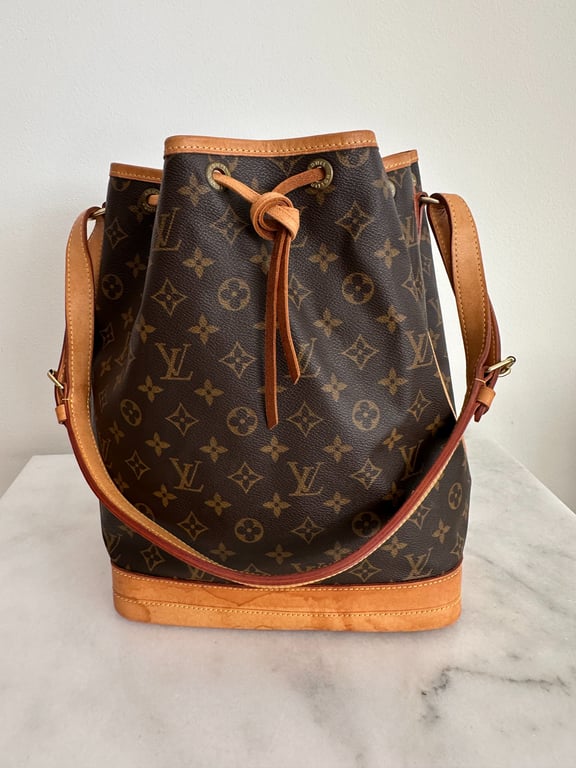 Brun Louis Vuitton skuldertaske i lærred med monogrammønster og lysebrune læderdetaljer, placeret på en marmorbordplade.