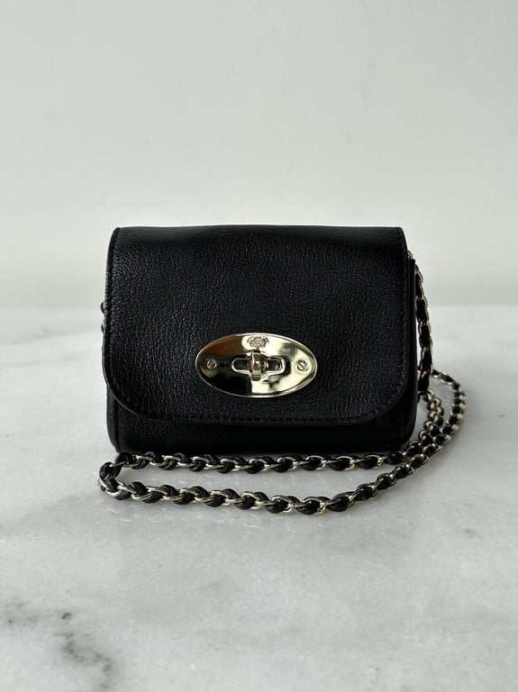 Sort lille lædertaske med kæde-rem og sølvfarvet lås, placeret på hvid marmorbord.