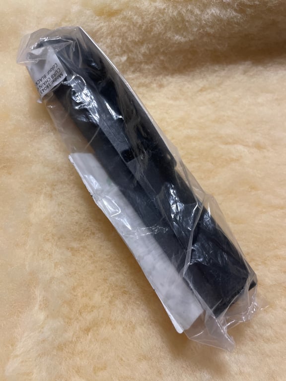 Sort bælte pakket ind i klar plastik på en beige overflade.