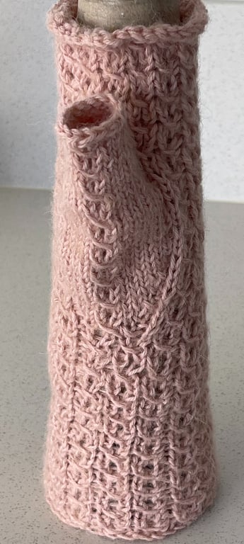 Strikket lyserød kagedåse med strukturmønster, vist på køkkenbord.