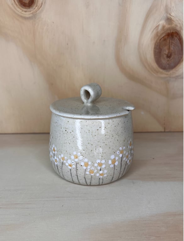 Keramisk sukkerskål med låg, dekoreret med små hvide og gule blomster på lysegrå baggrund.