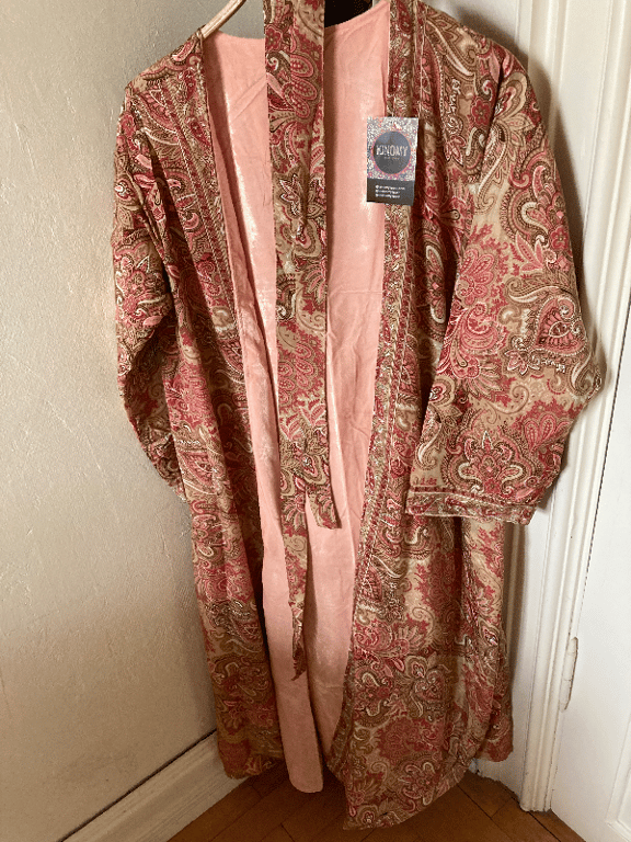Lyserød og beige kimono med paisleymønster hængende på en bøjle mod en lys væg. (2)