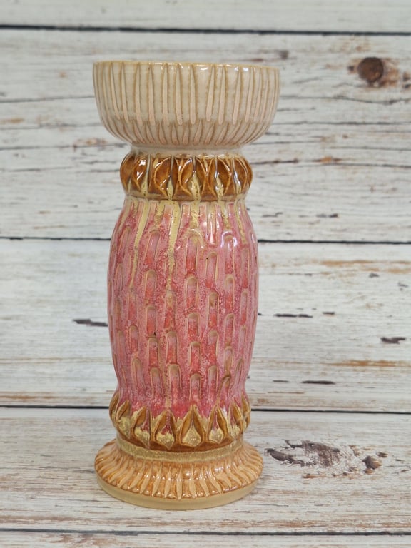Keramisk vase i beige, brun og pink med tekstureret mønster, placeret på træbord foran hvidt træpanel.