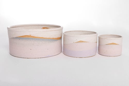 Tre keramiske krukker i forskellige størrelser med pastelfarvet landskabsdesign på en hvid baggrund.