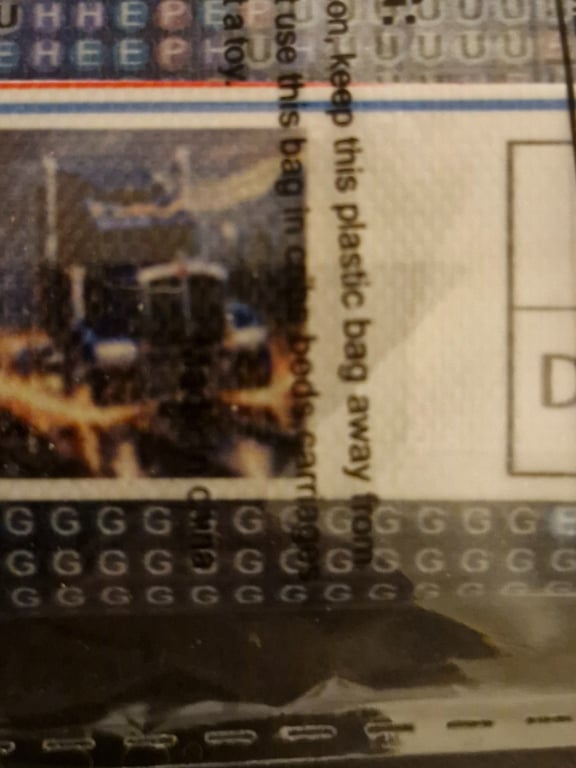 Nærbillede af et plastiklommetiket med tekst og et uskarpt billede af en bygning eller maskine bag plasticposen.