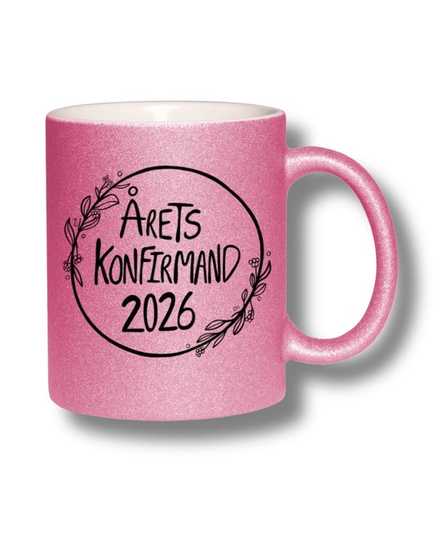 Pink glitrende kaffekop med teksten "Årets Konfirmand 2026" omgivet af en dekorativ krans af blomster og grene.