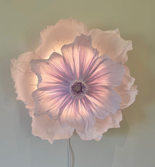 Blomstformet lampe med bløde, lyserøde kronblade, der lyser op mod en neutral væg. (1)