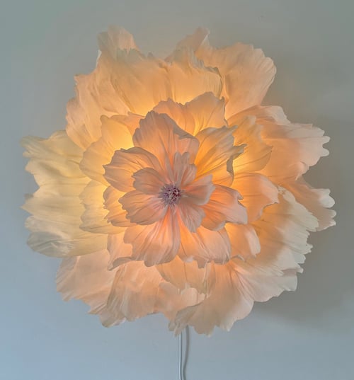 Blomstformet lampe med bløde, lagdelte hvide skærme, der udsender varmt, gyldent lys. (1)