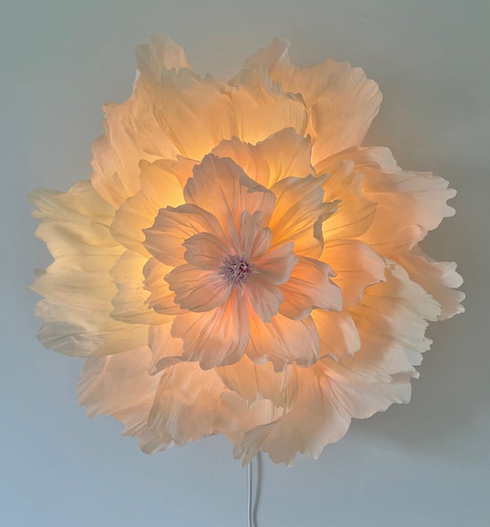 Blomstformet lampe med bløde, lagdelte hvide skærme, der udsender varmt, gyldent lys.