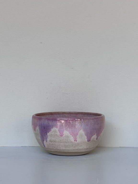 Lille keramisk skål med pink og hvide glasurdetaljer på en hvid overflade foran en hvid væg.