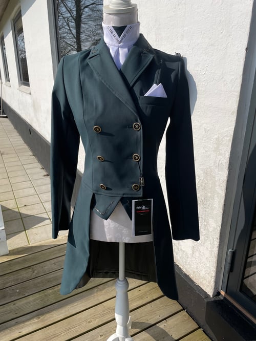 Mørkegrøn frakke med dobbeltradede knapper og halvlange forstykker på en mannequin, placeret udenfor mod en hvid væg. (1)