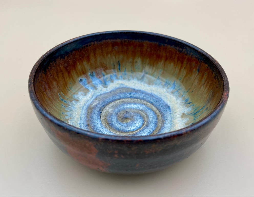 Keramisk skål med brune, blå og hvide farver og spiralformet mønster i bunden.