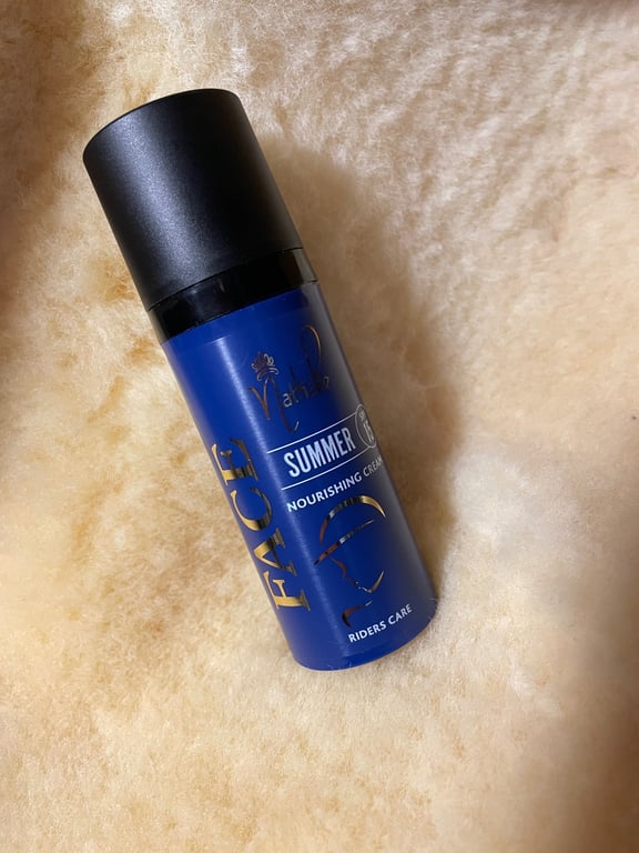 Billede af en blå flaske med sort låg mærket "FACE Summer Nourishing Cream" lagt på en lysebrun, blød pelslignende overflade.