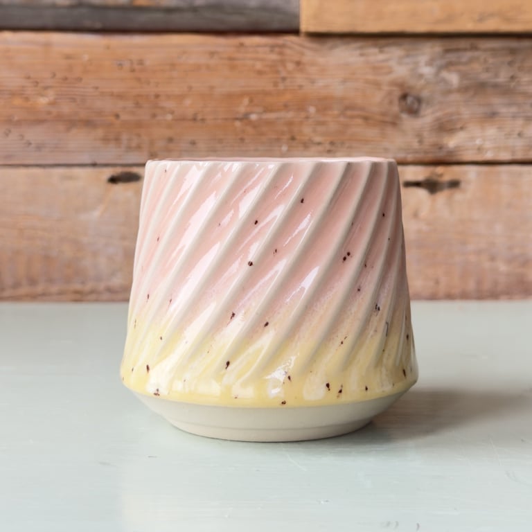 Lille keramikkrus med spiralformet mønster i lyserød og gul gradient på hvid bund, placeret på lys bordplade med træbaggrund.