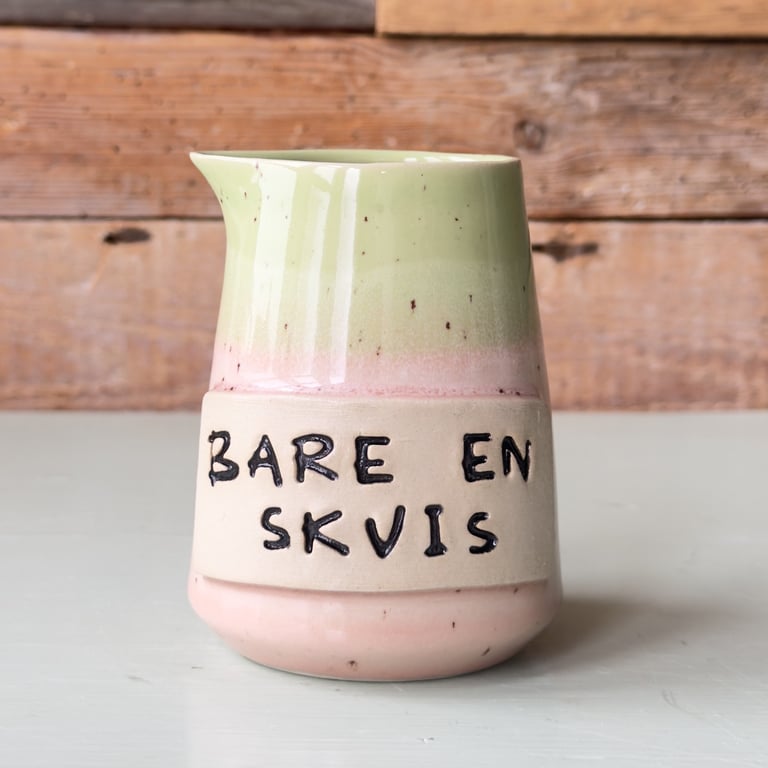 Keramikkande med grøn og lyserød glasur og tekst på dansk "Bare en skvis" på forsiden.