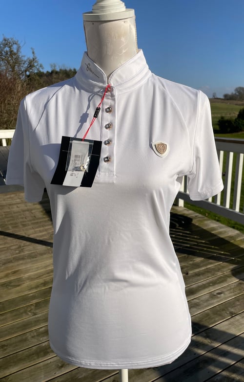 Hvid kortærmet sportspolo med knapper foran, vist på en mannequin udendørs på en træterrasse med blå himmel i baggrunden. (1)
