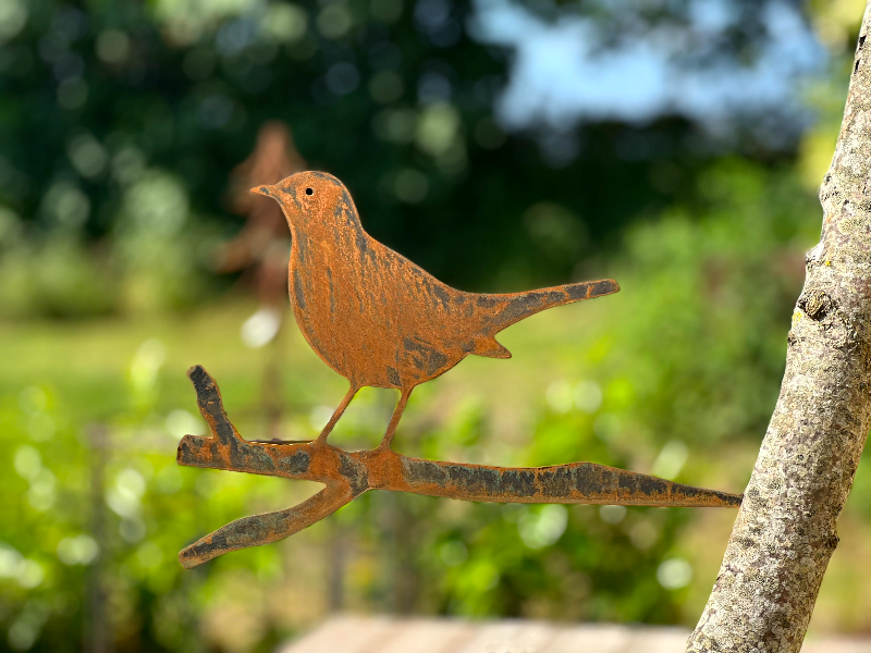 Rustfarvet metalfugl monteret på en gren med sløret grøn baggrund.