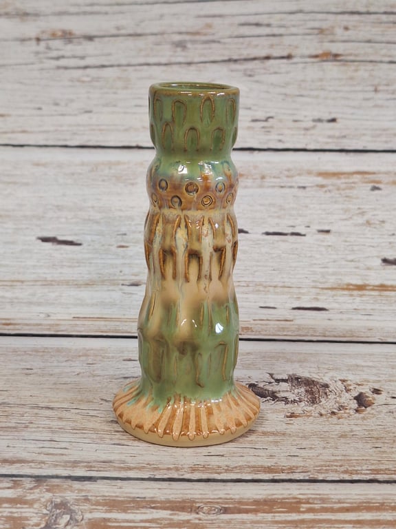 Keramisk lysestage med grønne og beige nuancer samt mønster, stående på træbord.