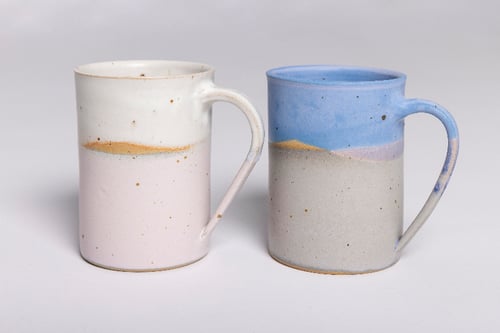 To forskellige keramiske krus med bølgede, to-tone glasurer i hvid, beige og blå.