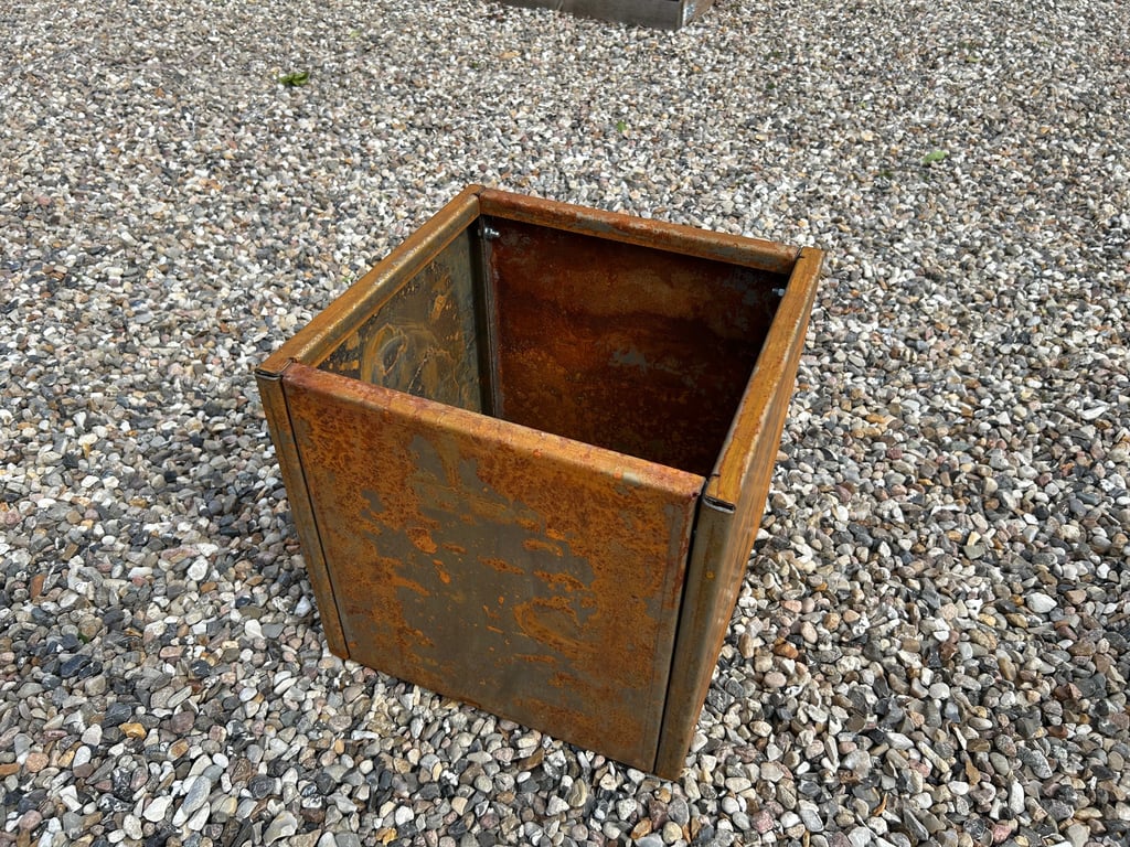 Rustent, firkantet metalkasse placeret på småsten.