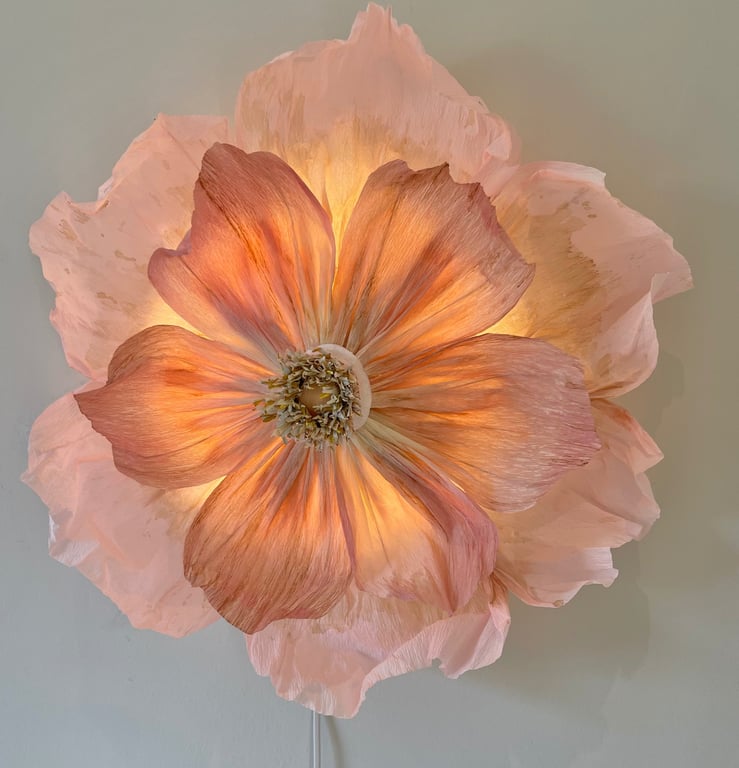 Stor dekorativ lampe formet som en lysende orange og lyserød blomst monteret på en væg.