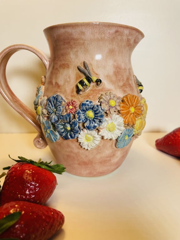 Lyserød keramikkande med farverige blomster og bier, omgivet af friske jordbær.