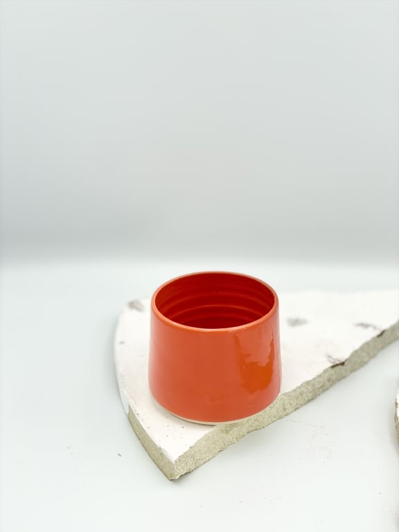 Rødt keramikkrus placeret på et flise- eller stykke betonstrimmel mod en hvid baggrund.
