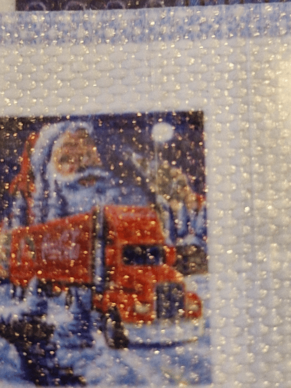 Nærbillede af et broderi med en juletrucks motiveret rød lastbil foran en julenisse og en måned på himlen.