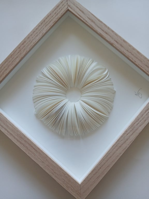 Billedram med en cirkulær skulptur lavet af foldede, hvide papirblade arrangeret i en donutform.